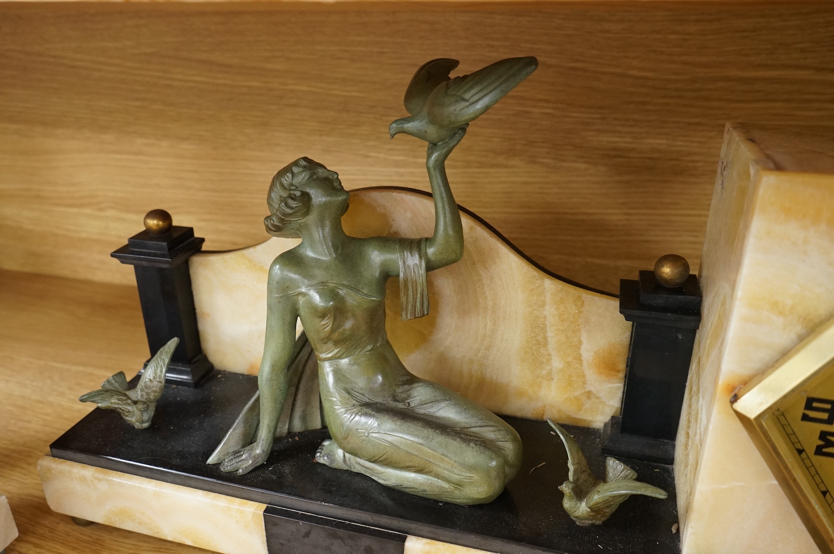 An Art Deco beige onyx and slate clock garniture surmounted with a seated girl holding a bird, 52cm wide
